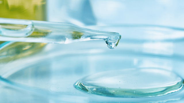 Close-up of a glass dropper releasing a clear liquid into a petri dish.