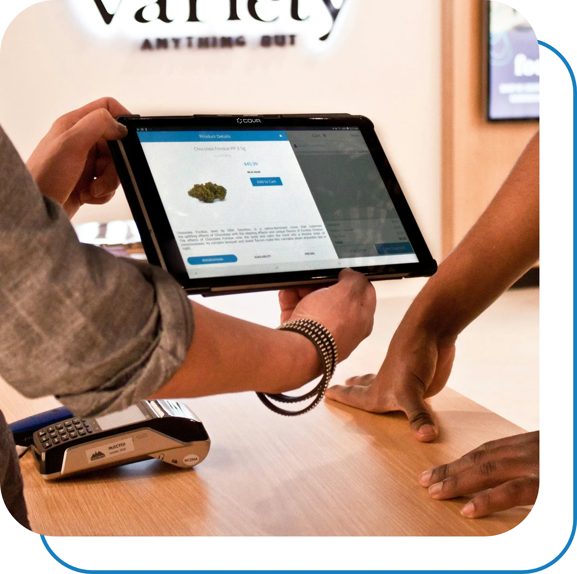 A person holds a digital tablet displaying an online product page featuring cannabis buds to another person across a counter. The background shows partially visible signage and a payment terminal on the counter. The scene indicates a cannabis dispensary transaction.